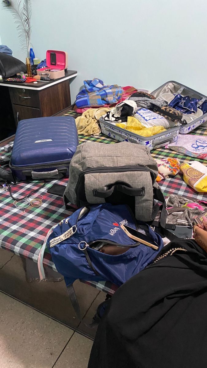 a person laying on a bed with luggage and other items scattered about it, including an open suitcase