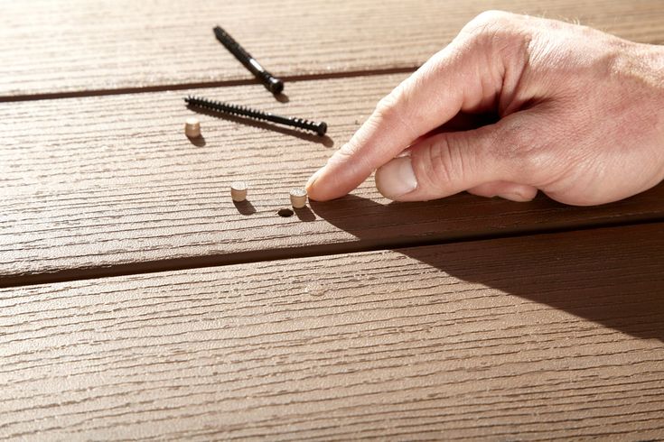 a person's hand is pointing at screws on a wooden table with nails