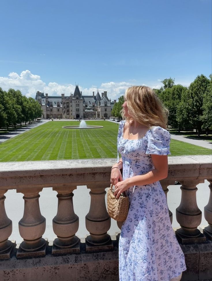 a woman in a dress is standing on a balcony looking at a large building with a lawn