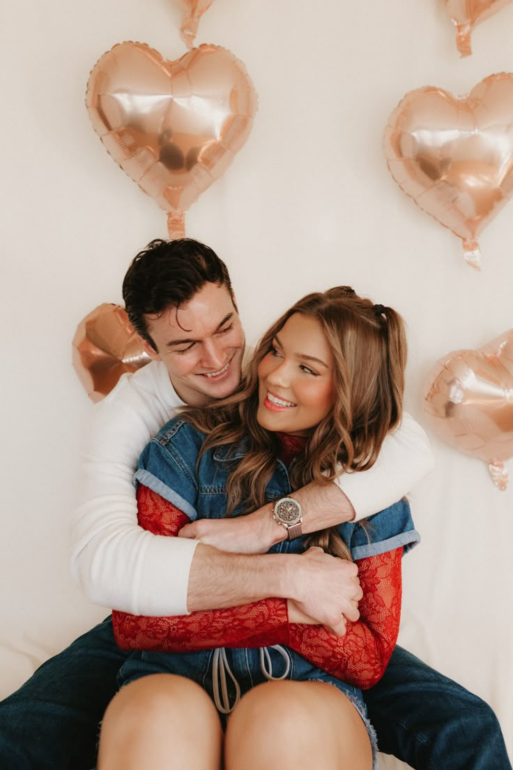 a man and woman sitting on top of each other in front of heart shaped balloons