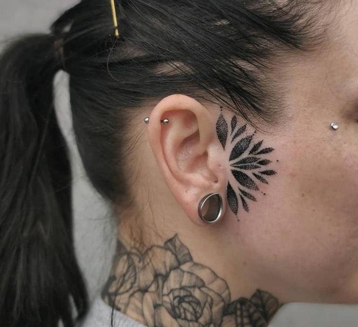 a woman with black tattoos on her neck and behind the ear is a rose tattoo