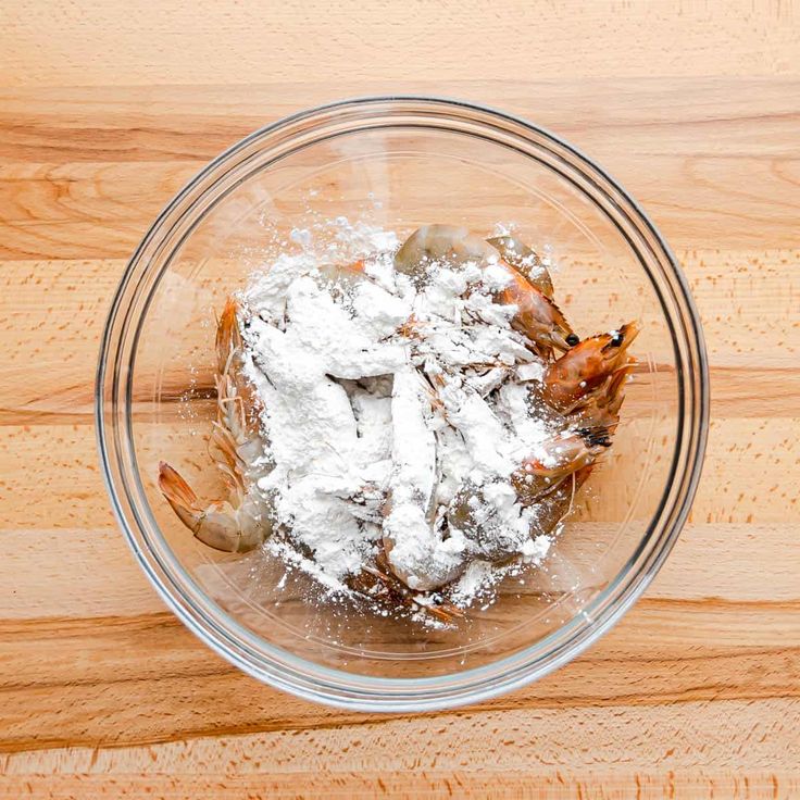 a glass bowl filled with powdered food on top of a wooden table next to a knife