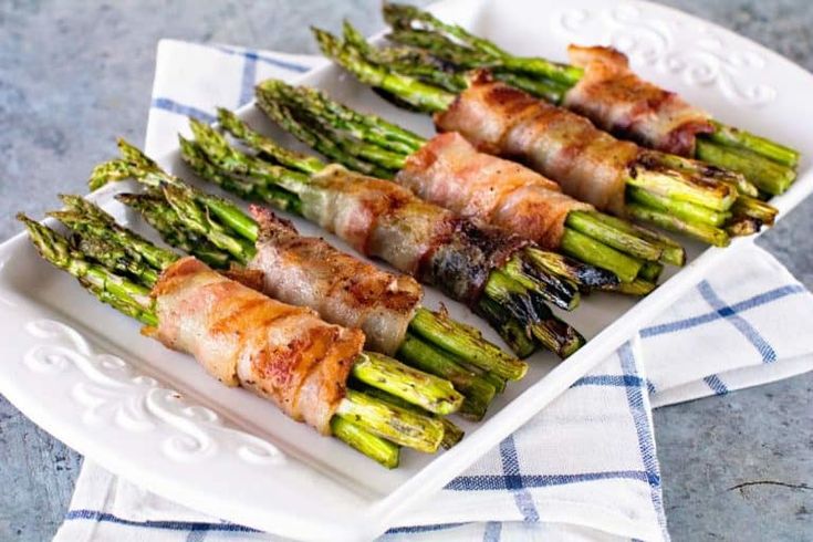 asparagus wrapped in bacon on a white plate with a blue and white towel