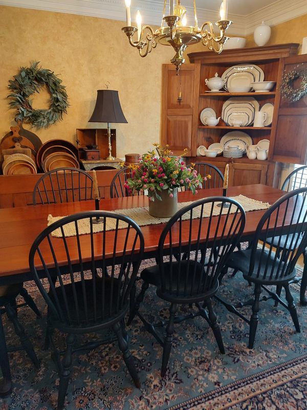 a dining room table with chairs and a vase on it's centerpiece in front of a china cabinet