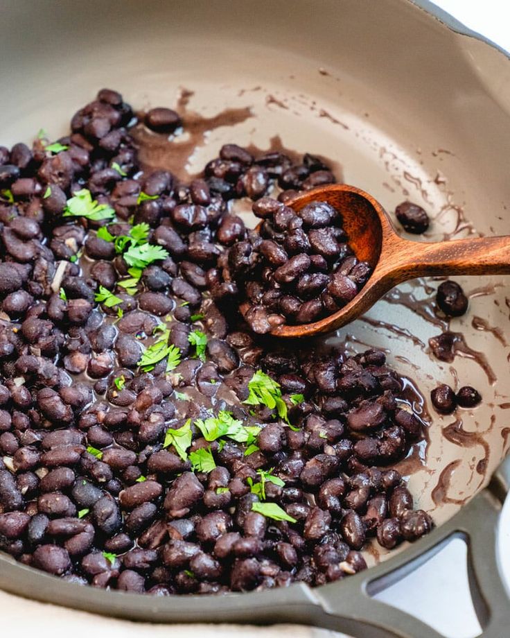 black beans are being cooked in a skillet with a wooden spoon on the side