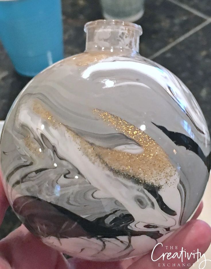 a hand holding a glass ornament with gold glitter on it