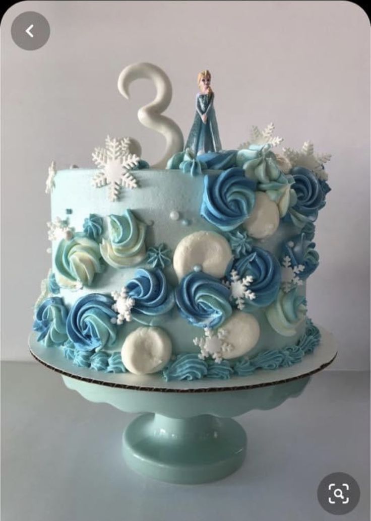 a blue and white frosted birthday cake with snowflakes on the top tier