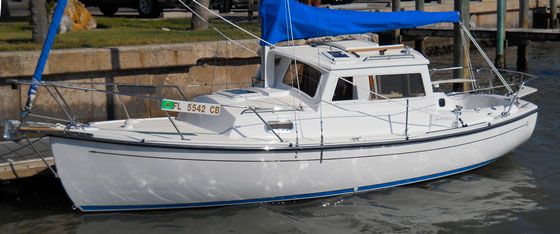 a white sailboat docked at a dock with blue tarp on it's side