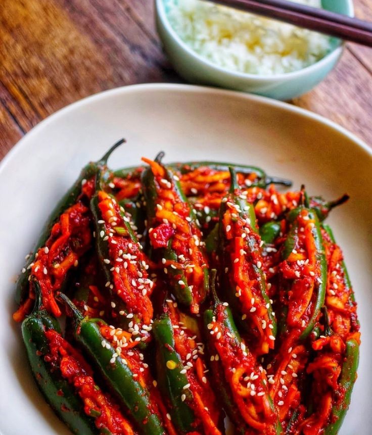 a white plate topped with green beans covered in red sauce next to chopsticks