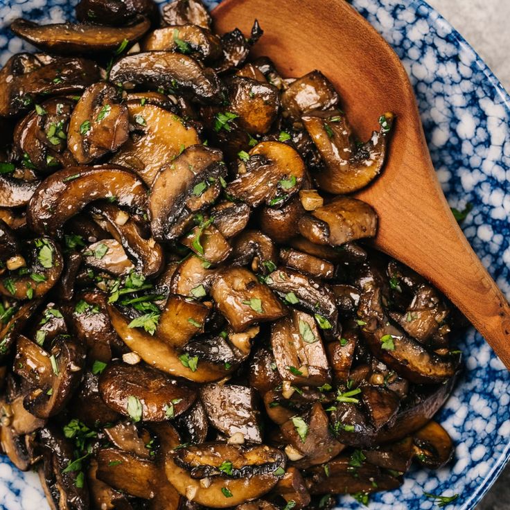 a blue and white bowl filled with mushrooms on top of a wooden spoon next to some parsley