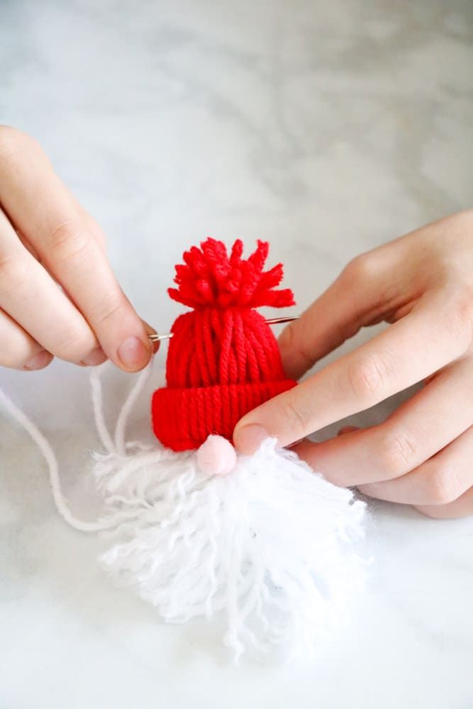 someone is knitting a small red hat with white yarn and thread on the table next to it