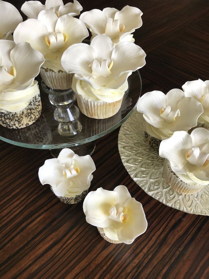 cupcakes decorated with white flowers on a glass plate and wooden table top next to each other