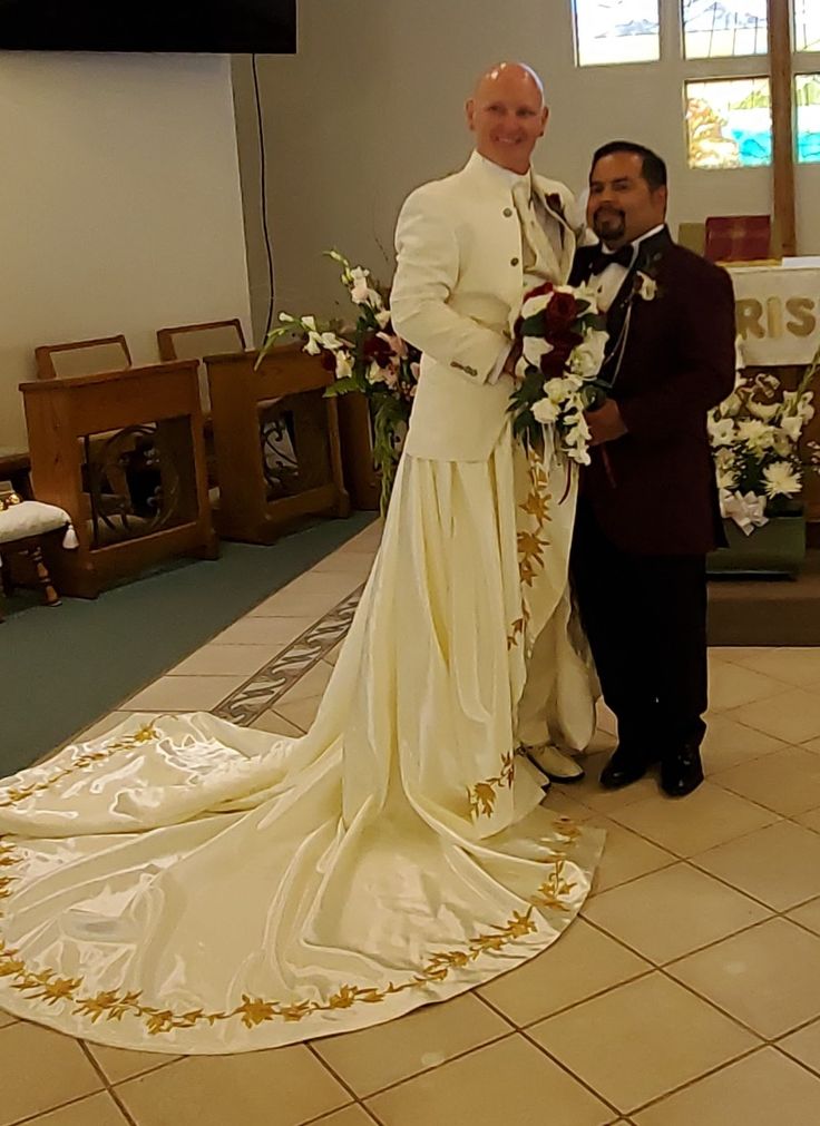 a man and woman in wedding attire standing next to each other with flowers on the floor