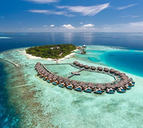 an island in the middle of the ocean with huts on it's sides and blue water