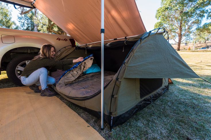 a woman sitting in the back of a truck next to a tent