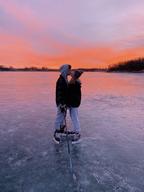 two people standing on ice with skis and poles in front of an orange sky