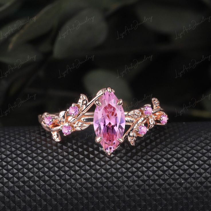 an image of a pink stone ring on a black surface with greenery in the background