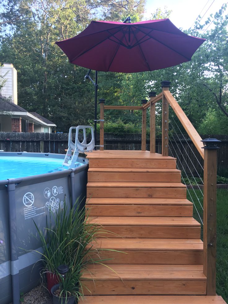 an above ground swimming pool with steps leading up to the deck and umbrella over it