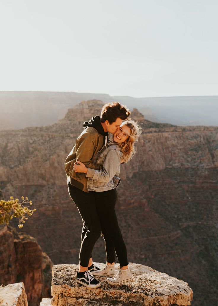 a man and woman hugging on the edge of a cliff in grand canyon national park