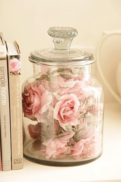 a glass jar with pink flowers sitting next to two books on a white table top