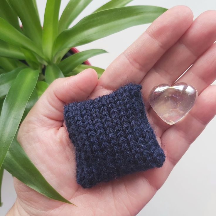 a hand holding a small blue knitted object with a spoon in it's palm