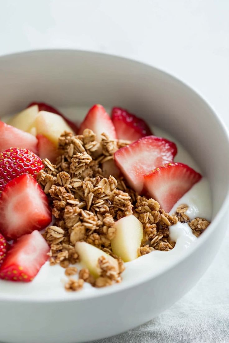 a bowl filled with granola and strawberries on top of a white table cloth