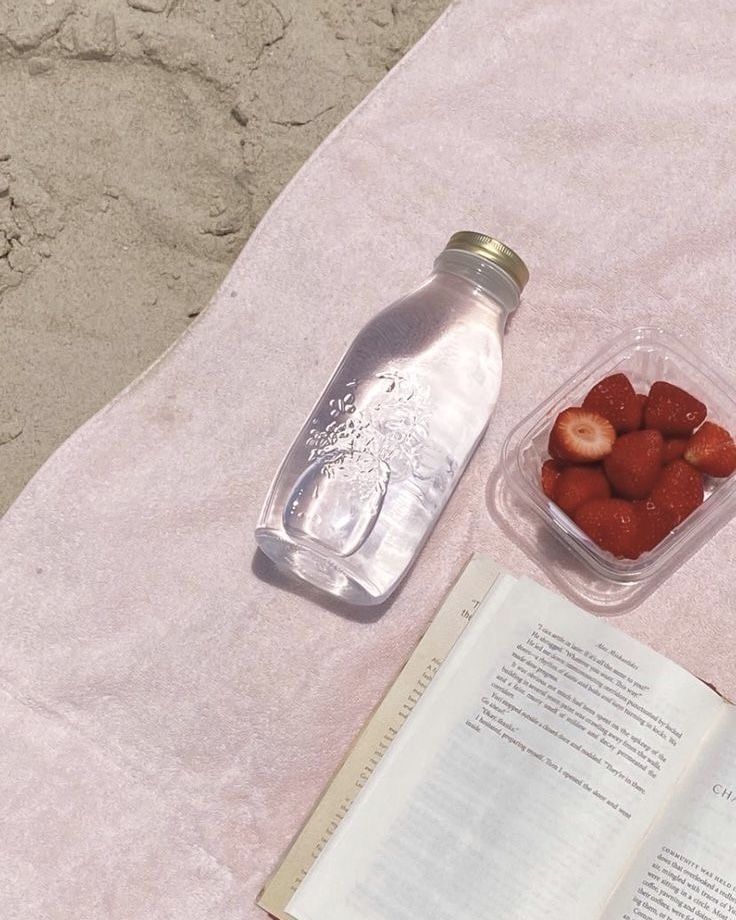 an open book and some strawberries on a towel next to a bottle of water