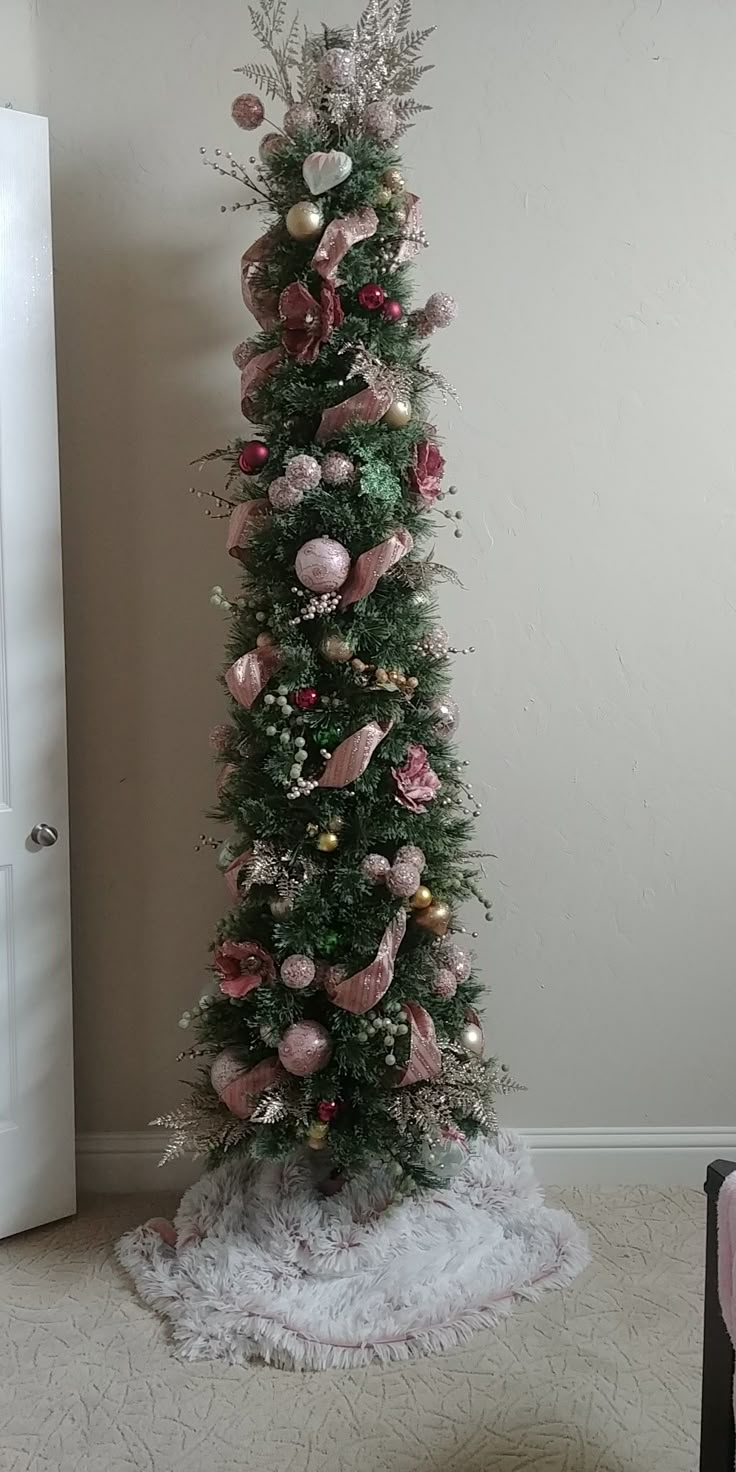 a decorated christmas tree with pink and gold ornaments on it in a room next to a white door