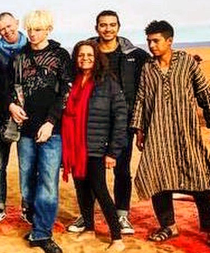 a group of people standing next to each other in the desert with sand dunes behind them