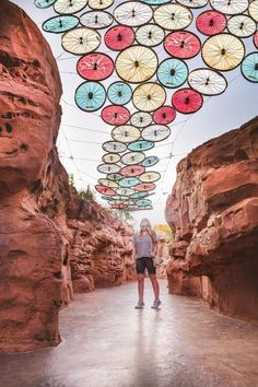 two people standing under colorful umbrellas hanging from the ceiling in a desert like setting