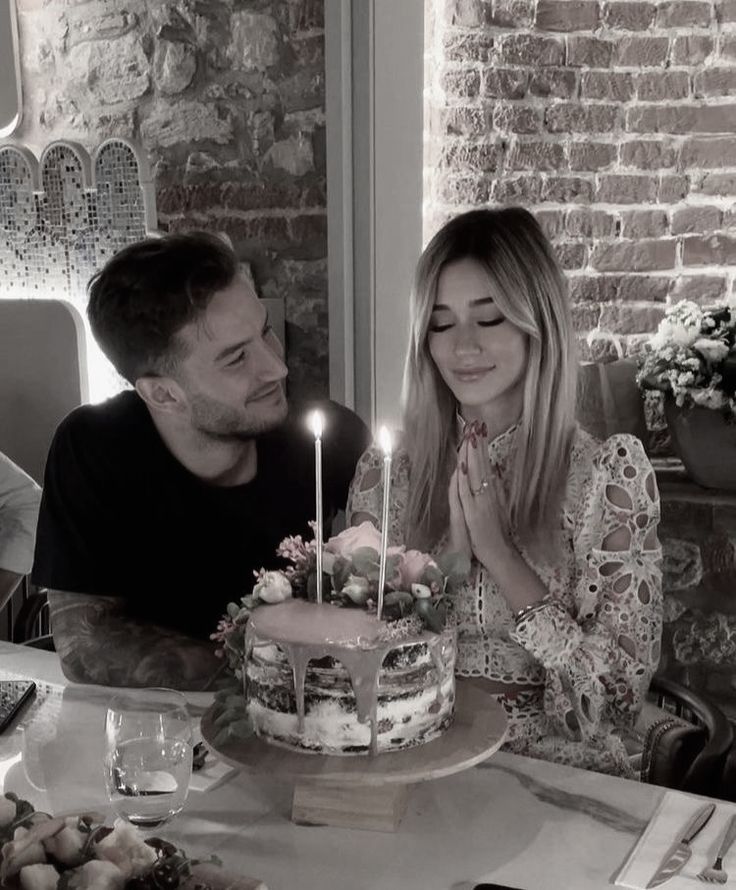 a man and woman sitting at a table with a birthday cake in front of them