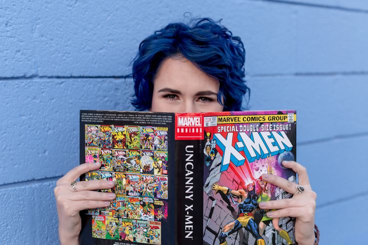 a woman with blue hair holding up a comic book