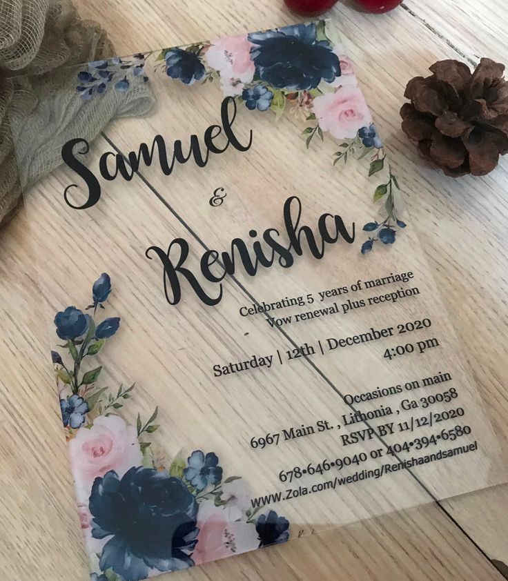 a wedding card with flowers and pine cones on the table next to it is an acrylic sign