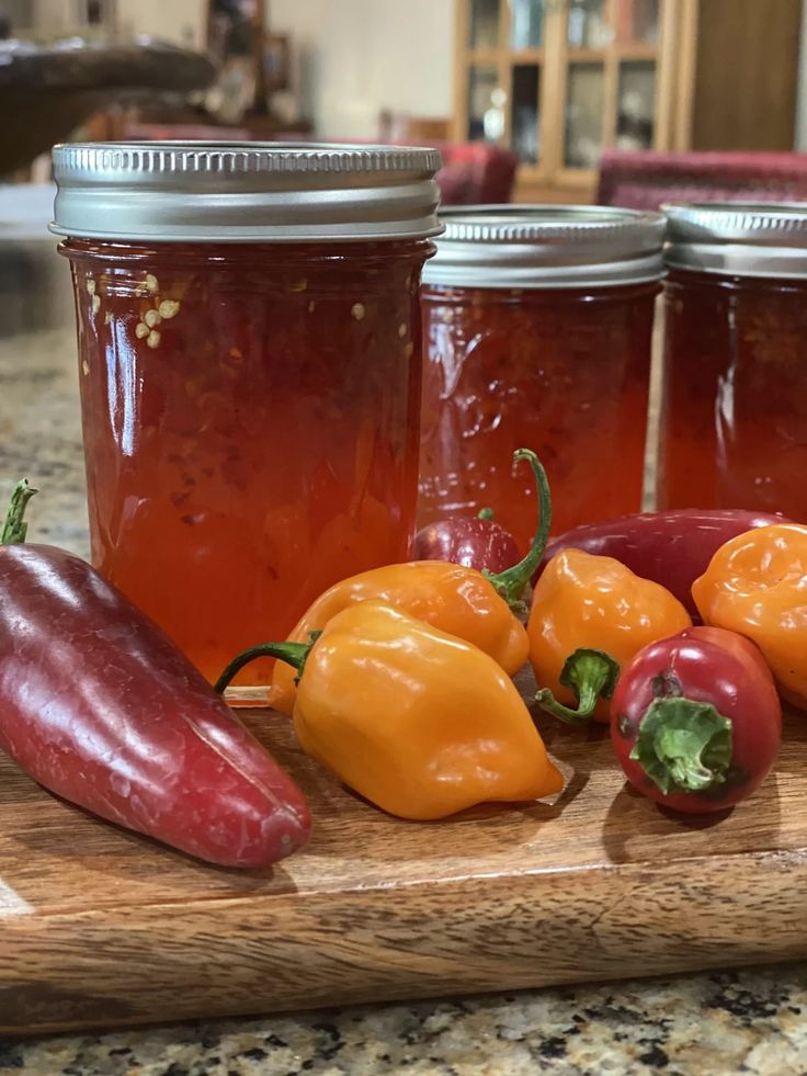 some red and yellow peppers on a cutting board next to jars of pickled vegetables