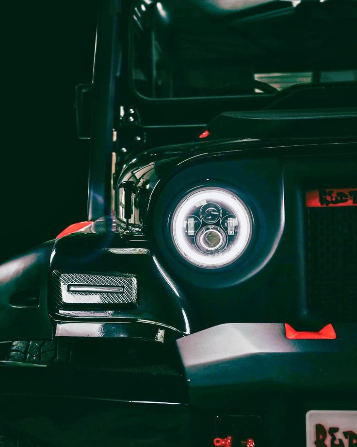 the front end of a black jeep with its lights on and red trimmings