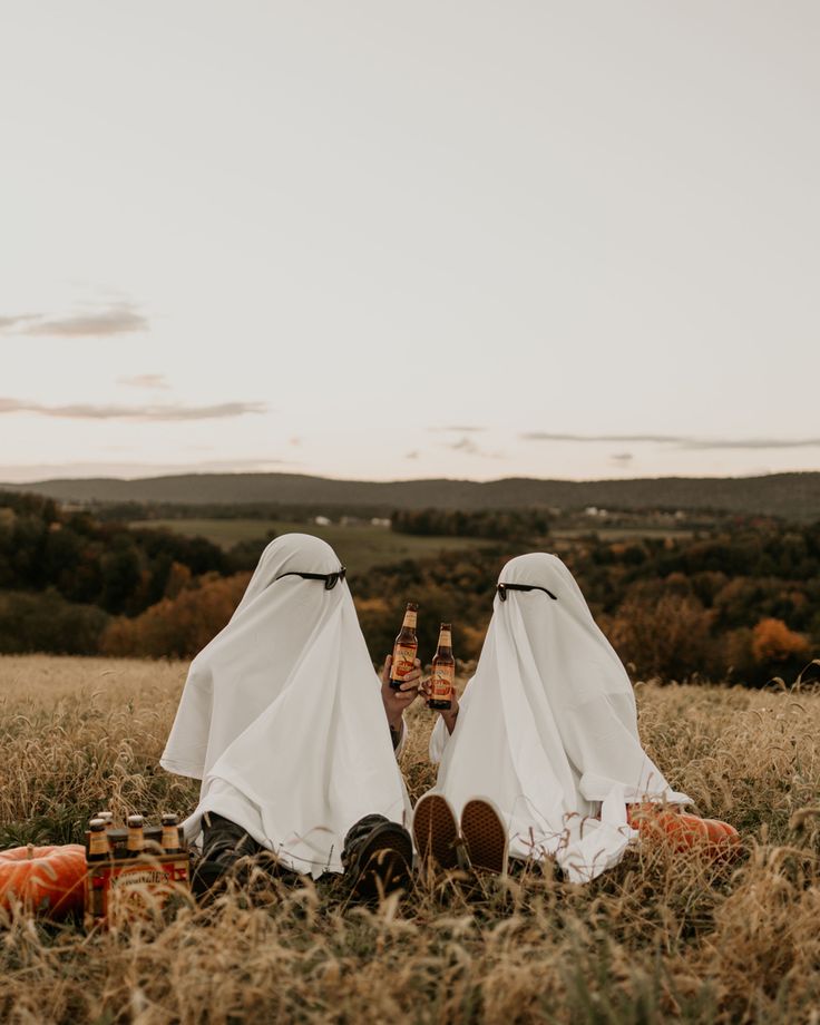 two people sitting in the grass with their heads covered by white cloths and holding beer bottles