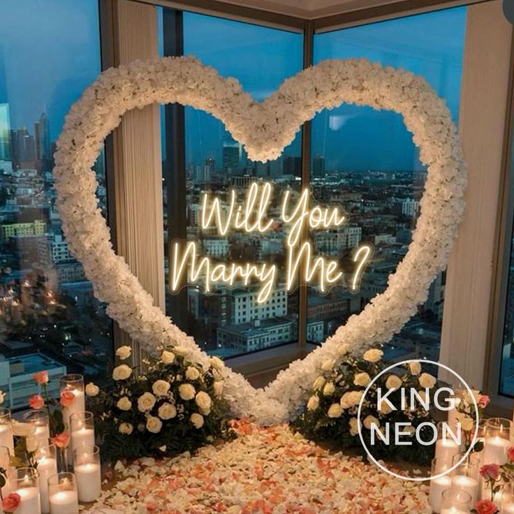 a heart shaped arrangement with candles and flowers in front of a window that says will you marry me?