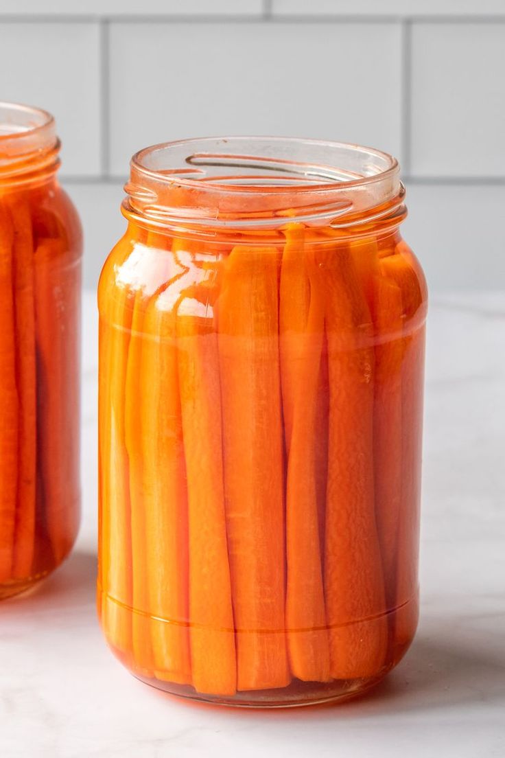 two jars filled with pickled carrots on top of a white counter next to each other