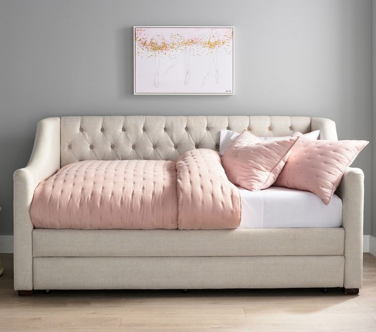 a white couch with pink pillows on it in front of a gray wall and wooden floor