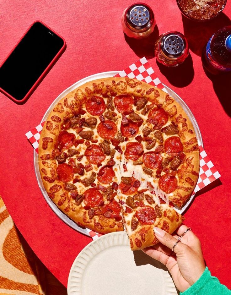 a pizza with pepperoni, sausage and cheese on a red tablecloth next to drinks