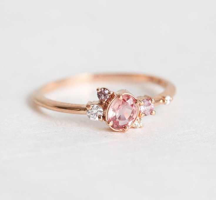 CAPELLA PEACH SAPPHIRE DIAMOND CLUSTER RINGCapella, an oval pink Sapphire engagement ring with accent Diamonds and Sapphires of different shades that was made to impress. Beautiful, unique and delicate, this design is the ultimate way of spoiling your loved one.DETAILSMain Stone  Stone: Sapphire  Shape: Oval  Color: Pink, Peach  Measurements: 5.1x3.4mm Side Stones  Round Sapphire: 2mm (1)  Round Sapphire: 1.5mm (1)  Round White Diamond: 2mm (1)  Round White Diamond: 1.35mm (1)  Round White Diamo Peach Sapphire Engagement Ring Rose Gold, Peach Sapphire Rings, Peach Sapphire Engagement Ring, Diamond Sapphire Engagement Ring, Sapphire Diamond Engagement, Gold Sapphire Ring, Peach Sapphire, Diamond Cluster Engagement Ring, Engagement Ring Rose Gold