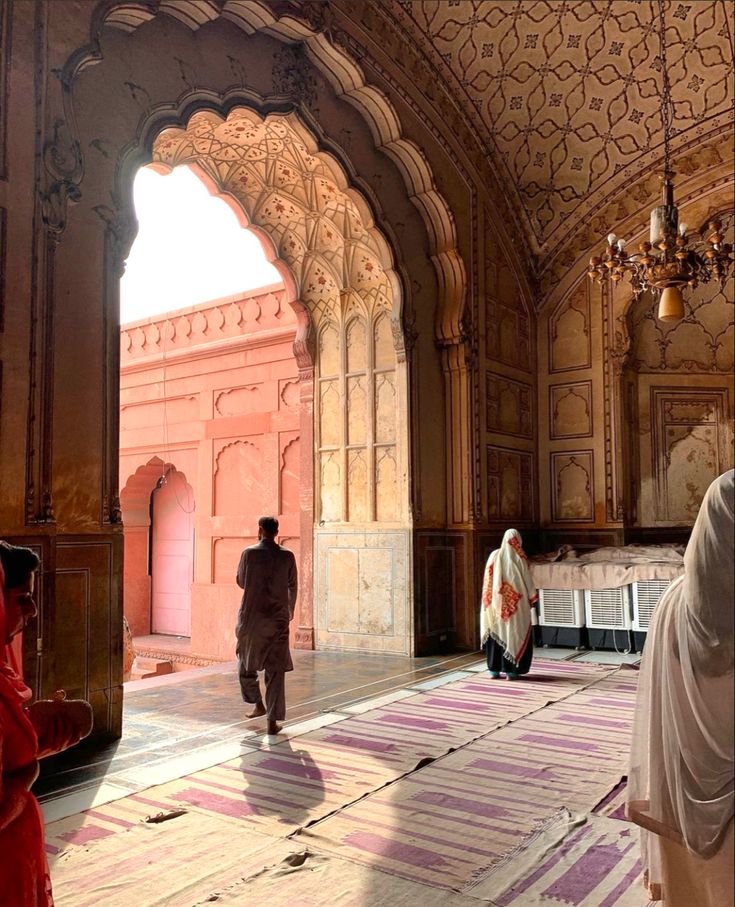 some people are walking around in an old building with pink and purple rugs on the floor