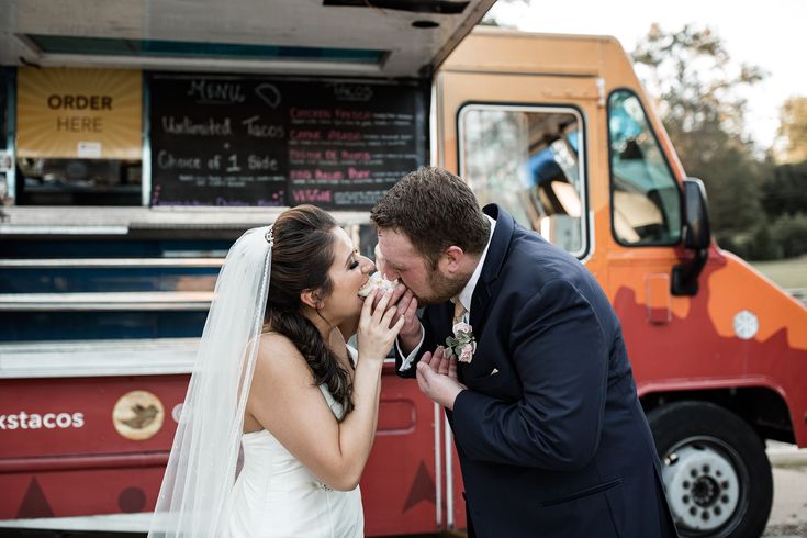 a bride and groom standing in front of a food truck with their hands on each other's lips