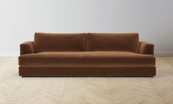 a brown couch sitting on top of a wooden floor next to a white wall in an empty room