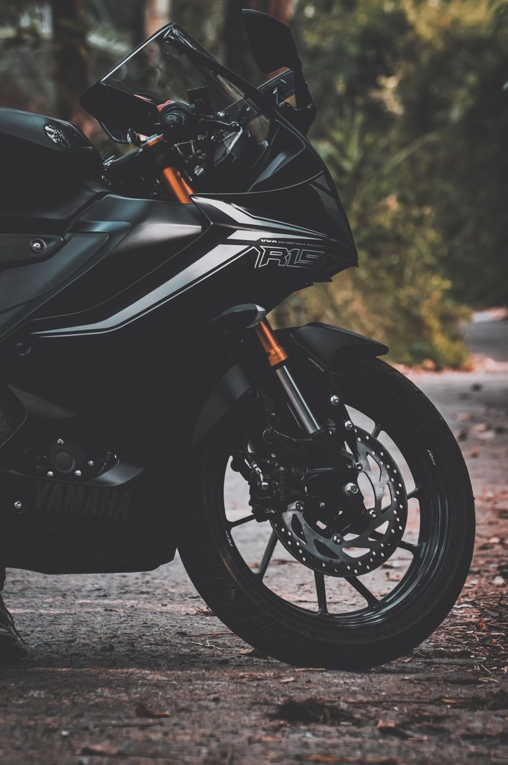 a black motorcycle parked on the side of a road next to some trees and bushes