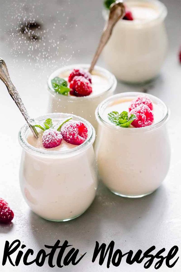 three desserts with raspberries and whipped cream in small glass jars on a table