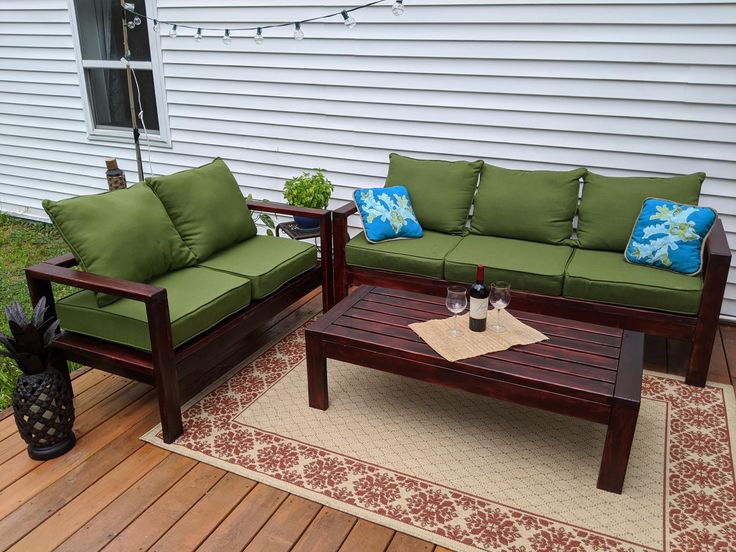 two couches and a coffee table sitting on a wooden deck in front of a house