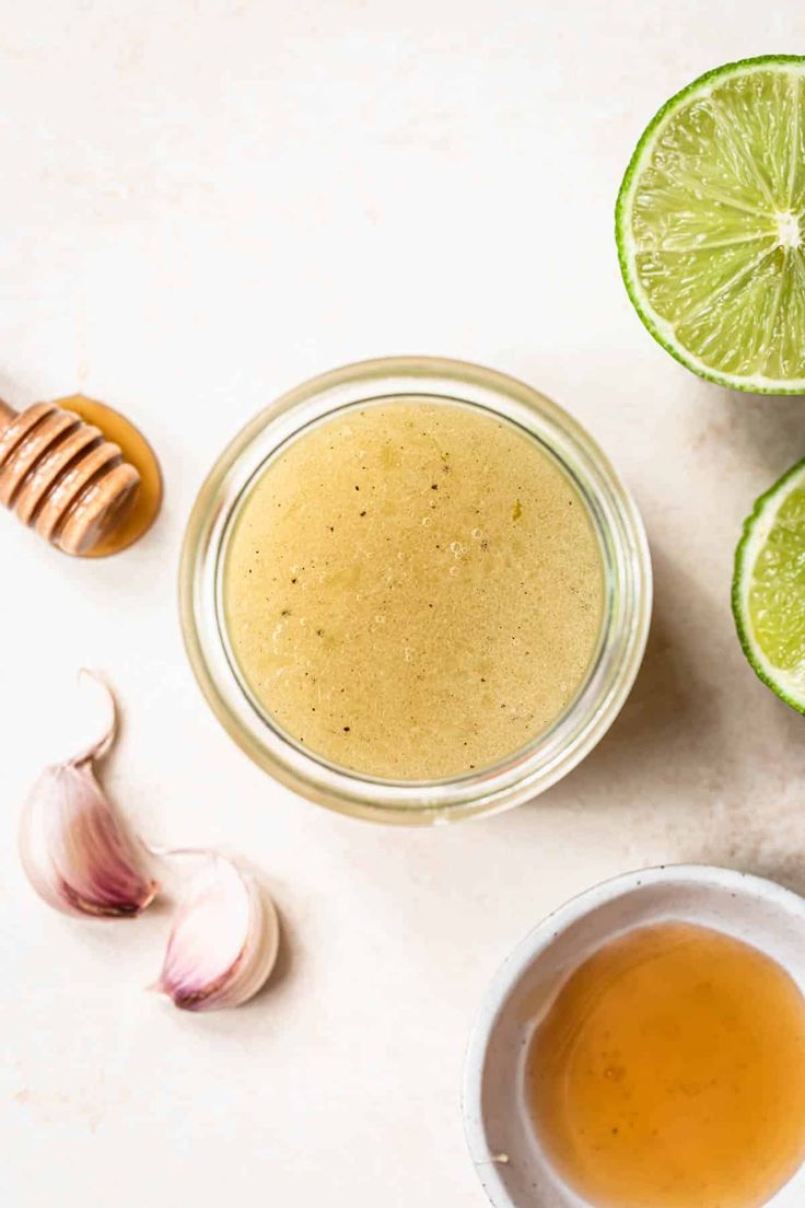 an overhead view of a bowl of honey, limes and garlic on a white surface