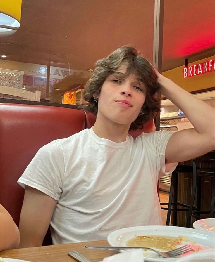 a young man sitting at a table in front of a plate of food with his hand on his head