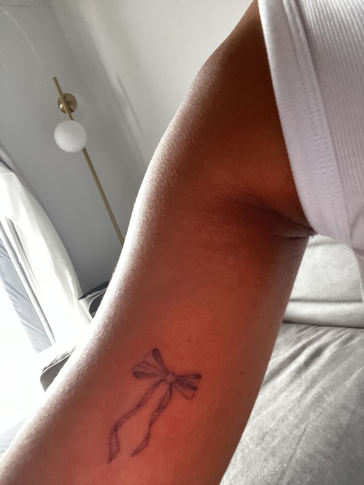 a woman's arm with a tattoo that has a small bow on the side